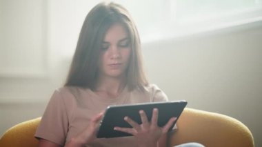 Genç kız tablet kullanıyor, hafta sonu evde tek başına oturuyor, modern aletli güzel bir genç bayanın portresi, internette sörf yapıyor, internetten alışveriş yapıyor, oradan mal sipariş ediyor, e-ticaret yapıyor ve uzaktan alışveriş yapıyor.