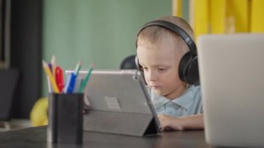 Şirin oğlan, eğitim ve gelişim karikatürlerini tablet ekranında izliyor, kulaklıkla dinliyor, evdeki ya da sınıftaki küçük oğlunun portresi, ebeveynlik ve gelişmekte olan çocuklar.