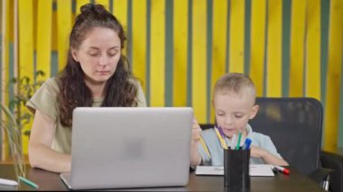 Çoklu görev yapan anne evde çalışıyor, annelik iznindeki kadın için serbest çalışıyor, dizüstü bilgisayarla daktilo yazıyor, sevimli küçük oğlu yaklaşıyor, meşgul anne ve anaokulu çocuğunun portresi masada.
