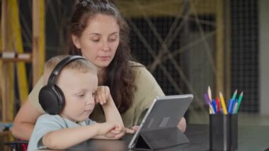 Anne ve küçük oğlu, modern dijital tablet sergilenen çizgi filmleri izliyorlar. Hafta sonları evde birlikte oturuyorlar. Elektronik aletleri olan mutlu bir aile, çocuklar için eğlence ve eğitim.