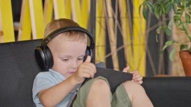 Evde tabletli ve kablosuz kulaklıklı meraklı küçük çocuk, anaokulu çocukları için online eğitim, internetteki eğlence ve eğlence, ebeveyn kontrol yazılımı, blok reklamları