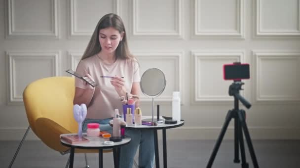 化妆艺术家提供了应用眼影的指导 她提建议时 用的是眼影调色板 女孩在三脚架上使用智能手机为选美博客创建内容 — 图库视频影像