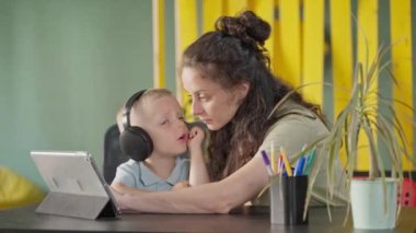 Evde tabletli ve kablosuz kulaklıklı küçük bir çocuk, anne ya da bebek bakıcısı çocuklar için çizgi film ya da eğitim videosu, öğrenme ve eğlence için modern cihazlar, bekar anne ve çocuk