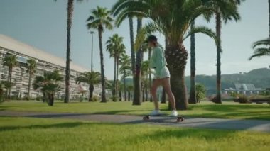 Yaz aylarında şehir sokaklarında sörf yapan genç bir kadın parkta kaykay sürüyor. Tropik palmiyelere ve parlak güneş ışığına karşı hareket ediyor. Havalı bir bayan spor hobisi yapıyor, tek başına paten kayıyor.