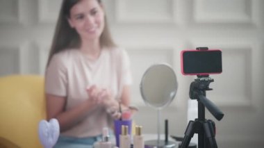 Neşeli kız vlogger akıntıyı bitiriyor ve bahsettiği güzellik ürünleri hakkında son sözlerini söylüyor. Tripoddaki akıllı telefona odaklan.