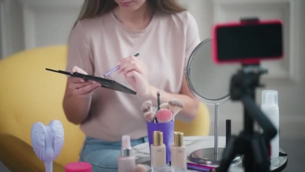 女性化妆师流淌着 并在应用眼色方面提供化妆指导 用三脚架把眼影调色板放在手机前的女孩 — 图库视频影像