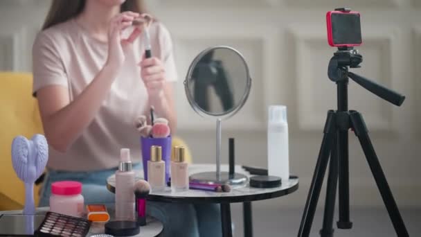 ソーシャルメディアのライブストリームで美容ブロガー プロの化粧アーティストは スマートフォンのカメラに化粧ブラシを示しています インフルエンサーは フォロワーのためのチュートリアルをお勧めしますし — ストック動画