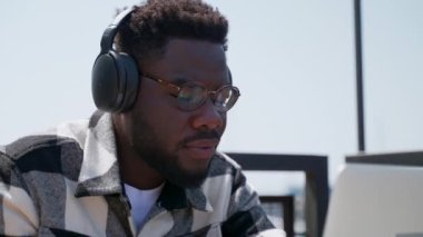 Afrikalı Amerikalı öğrenci kulaklıkla ses dinliyor ve dizüstü bilgisayarla çalışıyor, yakın plan portre, uzaktan ve e-öğrenerek serbest çalışma, İnternet üzerinden online eğitim