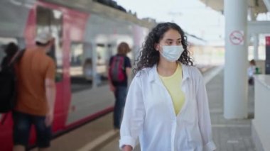 Geldikten sonra istasyonda maske takmış genç bir kadın yürüyor. Arka plandaki insanlar trene binecek. Virüs ve enfeksiyonu önlemek için yüz maskesi