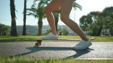 Yaz tatilinde uzun panoya binen genç bir kız, güvertede kadın ayaklarının yakın görüntüsü spor aktivitelerinde rahat etmek için spor ayakkabıları, kaykay süren genç bir kadın.