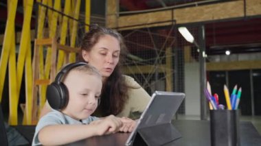 Küçük çocuk dijital tablette oyun öğreniyor. Anne onun hareketlerini izliyor ve kontrol ediyor. Elektronik eğitim faaliyetleri