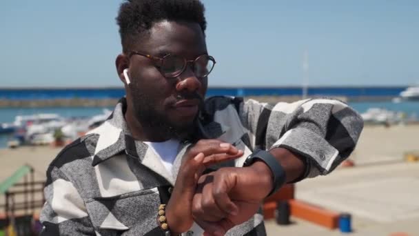 Νεαρός Αφροαμερικάνος Ασύρματα Ακουστικά Χρησιμοποιεί Smartwatch Του Για Τσεκάρει Νέα — Αρχείο Βίντεο