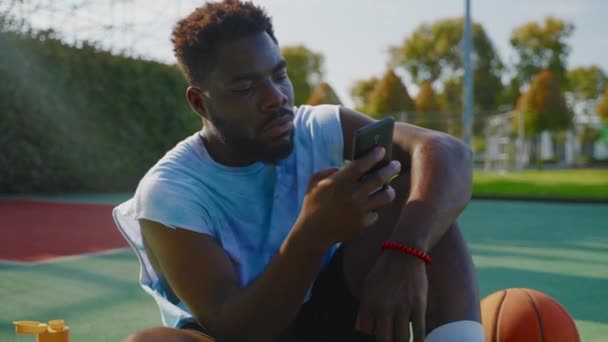 Africano Homem Americano Sentado Quadra Basquete Livre Usando Smartphone Para — Vídeo de Stock