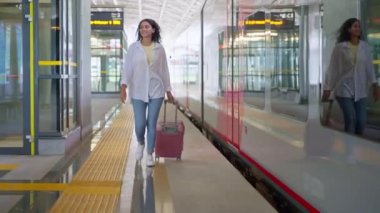 Bavullu mutlu kadın yolcu, yeni tren istasyonunda yürüyor. Ülkeyi boydan boya geziyor. Şehir sakinleri ve banliyö sakinleri için modern konforlu toplu taşıma.