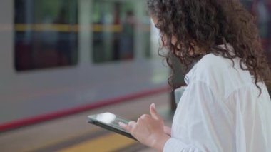 Genç bir kadın, platformda bekleyen tabletlerle internette sörf yapıyor, çevrimiçi alışveriş yapıyor, vitrindeki mağazaları geziyor, modern teknoloji, banliyö tren istasyonundaki kadın yolcu.