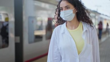 Yüz maskeli güzel bir kadının portresi tren peronunda, yolcuda ya da biriyle buluşuyor, Covid-19 salgını sırasında banliyö treniyle seyahat ediyor, enfeksiyon ve virüs yayılmasını engelliyor.