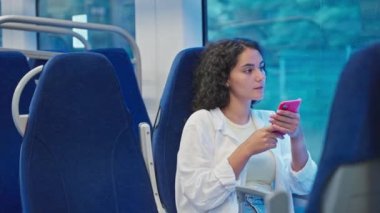 Güzel genç bir kadın trenle seyahat ediyor, pencerenin yanında oturuyor, elinde akıllı telefon, banliyö trenine binen kız öğrencinin portresi, içinde yolcu vagonu, pencereye bak.