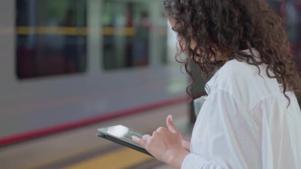 年轻女子通过平板电脑在站台等车 网上购物 浏览商店网站 现代技术 城郊火车站的女乘客等方式上网 — 图库视频影像