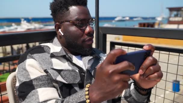 Young African American Man Wireless Earphones Using Mobile App Playing — Stock Video