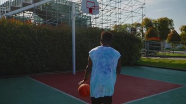 Siyah bir sporcunun açık havada antrenman yaparken yavaş çekim. Basketbolcu topu atıyor ve potaya mükemmel bir şekilde vuruyor.