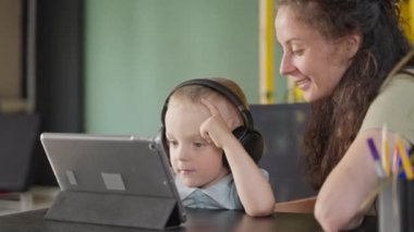 Küçük sevimli çocuk tablet ekranda çizgi film izliyor, kulaklıkla dinliyor, evde portre çekiyor, çocuklar için online eğitim videosu, modern elektronik aletlerle eğlence ve eğlence.