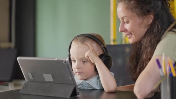 Γοητευτικό Μικρό Αγόρι Βλέπει Κινούμενα Σχέδια Στην Οθόνη Tablet Ακούγοντας — Αρχείο Βίντεο
