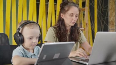 Annesi uzaktan evde çalışıyor ve küçük oğlu yanında çizgi film izliyor, anne ve bebeğin portresi, çağdaş aile, ebeveynlik izninde çalışan anne, serbest çalışma ve çocuklu kadınlar için yarı zamanlı iş.