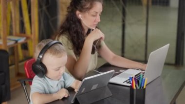 Küçük çocuk ve evde modern aletleri olan genç bir anne, kadın dizüstü bilgisayar kullanıyor, oğlu tabletle çizgi film izliyor, çağdaş yetişkinler ve çocuklar tarafından internet kullanımı, internet bağımlılığı