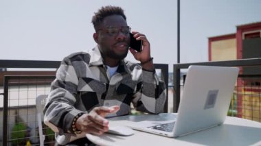 Kafede dizüstü bilgisayarı olan, cep telefonuyla konuşan, cep telefonuyla iletişim kuran, internetteki ve internetteki genç Afrikalı Amerikalı iş adamı, siyahi bir kişinin portresi.