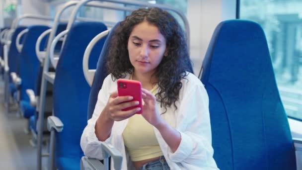 年轻的黑发姑娘 卷曲的头发乘火车通勤 在网上冲浪的漂亮女人在电话里消磨时光 — 图库视频影像