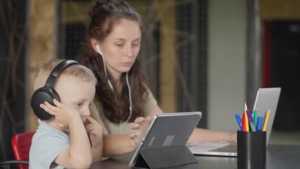 母はリモートで動作するようになるので 彼女はタブレットコンピュータ上の彼女の息子のための漫画やアプリを選択します 彼女は子供が静かだと何かに従事することができます — ストック動画