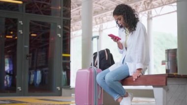 Banliyö trenlerinin boş platformunda yalnız bir kadın yolcu, akıllı telefonla bankta oturuyor ve internette sörf yapıyor, sosyal ağlardaki paylaşımları izliyor, banliyö trenini bekliyor, ülke çapında seyahat ediyor.