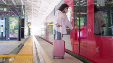 Bayan yolcu bavul ve yüz maskesi ile banliyö treninin kapılarını açıyor, vagona biniyor, Covid-19 salgını sırasında tren yoluyla seyahat ediyor, modern tren istasyonu terminali.