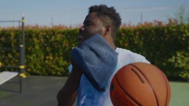Açık hava basketbol antrenmanından sonra yüzü havluyla silen Afro-Amerikalı bir adam. Sağlık ve eğlence için spor