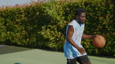 Afrika kökenli Amerikalı bir adamın saha dışında basketbol antrenmanı yaparken yavaş çekim. Top sürüyor ve şut çekiyor. Hobi ve yaşam tarzı olarak spor