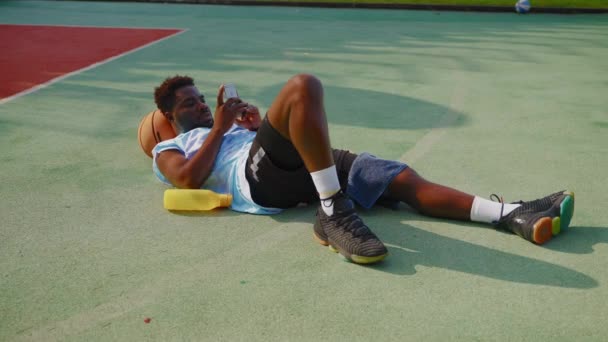 Afroamerikaner Ruht Sich Nach Dem Training Auf Dem Basketballfeld Aus — Stockvideo