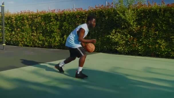 屋外裁判所でバスケットボールを練習している若いアフリカ系アメリカ人男性のスローモーションショット 彼はボールをドリブルし それを撃つが フープを逃す — ストック動画