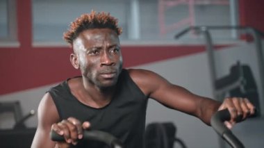 Güçlü siyah adam hava bisikleti üzerinde egzersiz yapıyor. Atletik sporcu kaslı kollarıyla bisiklet sürüyor ve hareket ediyor. Crossfit egzersizi