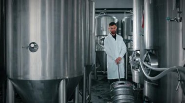 Büyük paslanmaz çelik tankları olan modern bira fabrikası ve bir fıçı bira yuvarlayan el arabası olan işçi. Gıda ve içecek üretim tesisleri