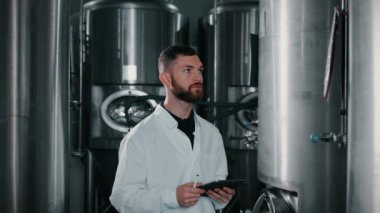 Erkek gıda teknisyeni fabrikada devriye geziyor. Paslanmaz çelik işleme tankları hakkındaki bilgileri kontrol ediyor ve dijital tablet üzerine notlar alıyor. Yiyecek ve içecek üretimi