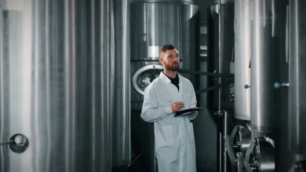 技術者は現代の醸造所の発酵部門を歩き 円筒形の円錐形の発酵タンクのデータを見ています — ストック動画