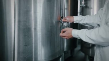Gıda teknisyeni bira fabrikasındaki paslanmaz çelik tanktan bardağa siyah bira döküyor. İçecek üretimi