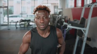 Siyah bir sporcunun kardiyo çalışması yaparken yakın plan portresi. Koşu bandında koşarken kameraya odaklanmış bir adam