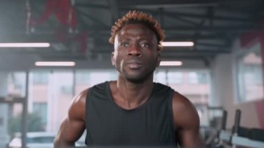Spor merkezinde çalışan Afrikalı bir Amerikalının yavaş çekim ön çekimi. Sporcu kardiyo eğitimi alıyor ve koşu bandında koşuyor.