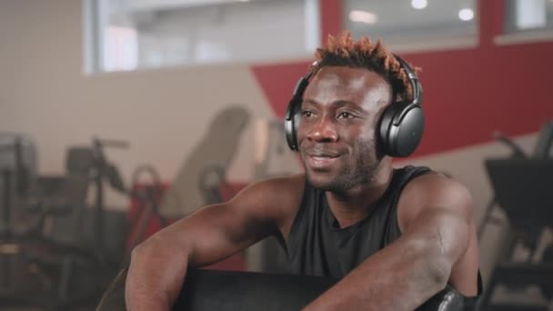 在体育中心锻炼期间休息一下的非洲裔美国人 运动员在无线耳机中听最喜欢的音乐 — 图库视频影像