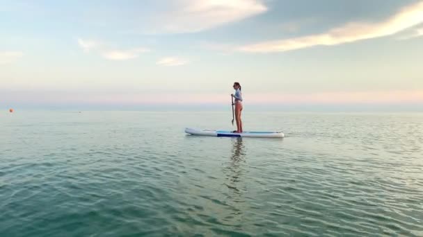 穏やかなシアン海の水と1人の女性がアップボードに浮かんで パドルで漕いで 夜空に対する風光明媚な景色 リラックスした水の活動 — ストック動画