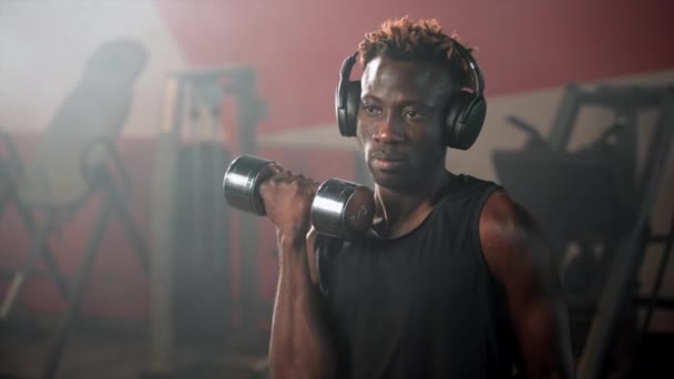 慢镜头的运动非裔美国人在健身房与音乐一起锻炼 他在无线耳机里用哑铃练习 — 图库视频影像