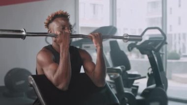 Vücut geliştirme merkezinde kol ve omuzlarını kaldıran siyah kaslı bir sporcunun yavaş çekim çekimi. Sağlıklı ve güçlü bir vücut oluşturmak için spor yapıyor.