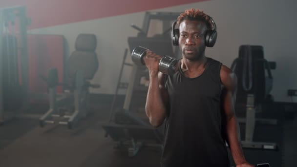 重点运动员加强手臂与哑铃二头肌卷曲 非裔美国人在耳机里做运动和欣赏音乐 — 图库视频影像