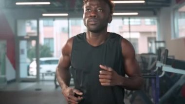 Afrikalı kaslı Amerikalı adam spor salonunda koşu bandında koşuyor, fitness merkezinde portre çekiliyor, formda ve spor aktivitelerini iyi vücut şekline getiriyor, spor salonunda atletik siyahi adam eğitimi alıyor.